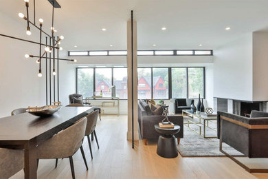 This is an example of a mid-sized contemporary open concept living room in Toronto with white walls, light hardwood floors, a standard fireplace, a tile fireplace surround, a wall-mounted tv, beige floor and wood walls.