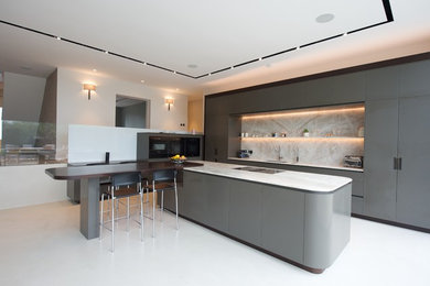 Design ideas for an expansive contemporary l-shaped kitchen in Surrey with flat-panel cabinets, granite benchtops, black appliances, concrete floors, with island, an undermount sink, grey cabinets, white splashback, white floor and white benchtop.