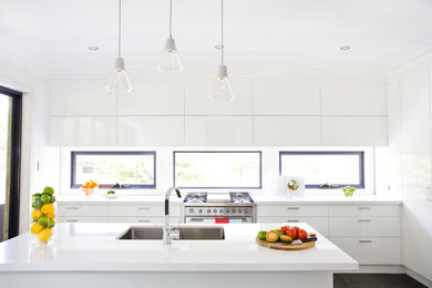 Photo of a mid-sized contemporary galley open plan kitchen in Melbourne with a double-bowl sink, white cabinets, white splashback, stainless steel appliances and with island.