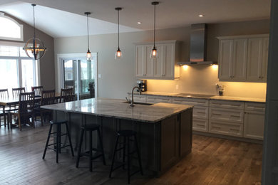 Example of a transitional medium tone wood floor kitchen design in Toronto with recessed-panel cabinets, granite countertops, stainless steel appliances and an island