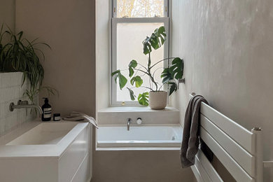 Design ideas for a small scandinavian family bathroom in Edinburgh with flat-panel cabinets, white cabinets, a built-in bath, a shower/bath combination, a wall mounted toilet, white tiles, mosaic tiles, beige walls, a wall-mounted sink, solid surface worktops, beige floors, an open shower, white worktops, a wall niche, a single sink and a floating vanity unit.