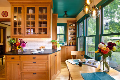 Inspiration for a mid-sized traditional l-shaped eat-in kitchen in Minneapolis with a farmhouse sink, beaded inset cabinets, medium wood cabinets, soapstone benchtops, white splashback, subway tile splashback, stainless steel appliances, light hardwood floors, brown floor, black benchtop and wood.