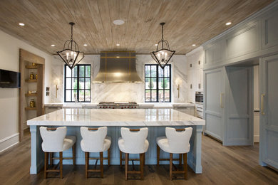 This is an example of an expansive traditional l-shaped open plan kitchen in Atlanta with a farmhouse sink, recessed-panel cabinets, white cabinets, marble benchtops, white splashback, marble splashback, stainless steel appliances, light hardwood floors, with island, brown floor and white benchtop.