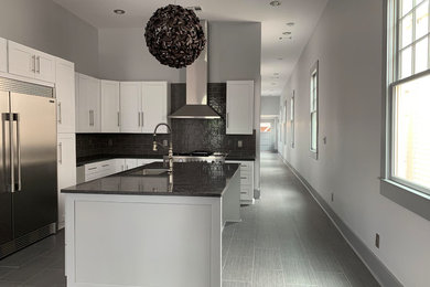 Small transitional l-shaped gray floor kitchen photo in New Orleans with an undermount sink, shaker cabinets, white cabinets, black backsplash, subway tile backsplash, stainless steel appliances, an island and black countertops