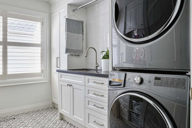 Inspiration for a transitional porcelain tile laundry room remodel in Toronto with an undermount sink, white cabinets, white backsplash, subway tile backsplash, a stacked washer/dryer and black countertops