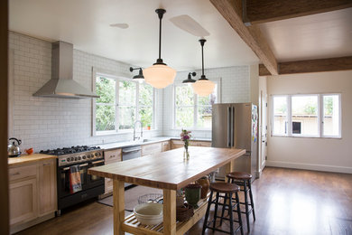Example of a large farmhouse l-shaped dark wood floor and brown floor eat-in kitchen design in San Francisco with an undermount sink, shaker cabinets, light wood cabinets, wood countertops, white backsplash, subway tile backsplash, stainless steel appliances and an island
