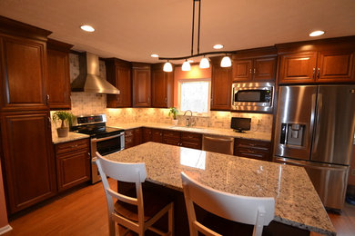 Inspiration for a mid-sized transitional l-shaped medium tone wood floor eat-in kitchen remodel in Columbus with an undermount sink, raised-panel cabinets, dark wood cabinets, granite countertops, beige backsplash, stone tile backsplash, stainless steel appliances and an island