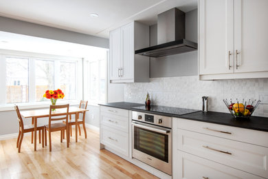 Example of a mid-sized transitional u-shaped light wood floor, beige floor and coffered ceiling eat-in kitchen design in Ottawa with an undermount sink, shaker cabinets, white cabinets, solid surface countertops, white backsplash, porcelain backsplash, stainless steel appliances, no island and black countertops