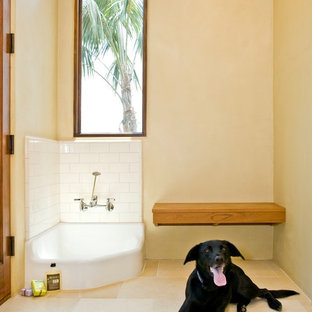 サンタバーバラの大きいトロピカルスタイルのおしゃれな家事室 (黄色い壁、ベージュの床、アンダーカウンターシンク、シェーカースタイル扉のキャビネット、白いキャビネット、トラバーチンの床、左右配置の洗濯機・乾燥機、白いキッチンカウンター) の写真