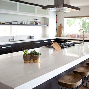 Contemporary eat-in kitchen ideas - Example of a trendy medium tone wood floor eat-in kitchen design in San Diego with a drop-in sink, glass-front cabinets, stainless steel cabinets, quartz countertops, white backsplash, stainless steel appliances and an island