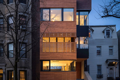 This is an example of a large modern three-storey townhouse exterior in New York with wood siding, a flat roof and a mixed roof.