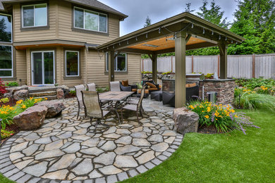 Large modern backyard patio in Seattle with an outdoor kitchen, natural stone pavers and a gazebo/cabana.