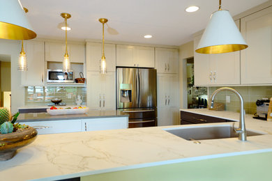 Example of a mid-sized trendy u-shaped medium tone wood floor and brown floor open concept kitchen design in Minneapolis with an undermount sink, shaker cabinets, white cabinets, quartz countertops, yellow backsplash, glass tile backsplash, stainless steel appliances, an island and white countertops