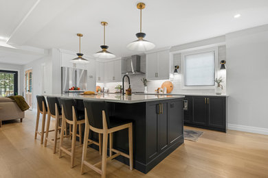 Large transitional l-shaped light wood floor and beige floor eat-in kitchen photo in Ottawa with shaker cabinets, white cabinets, quartz countertops, white backsplash, ceramic backsplash, stainless steel appliances, an island and white countertops