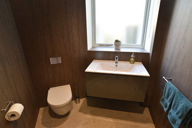 Photo of a medium sized modern cloakroom with flat-panel cabinets, grey cabinets, a wall mounted toilet, brown tiles, porcelain tiles, brown walls, porcelain flooring and a wall-mounted sink.