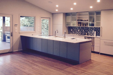 Minimalist medium tone wood floor kitchen photo in Other with flat-panel cabinets, white cabinets, quartzite countertops, metallic backsplash, stainless steel appliances and a peninsula