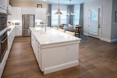 Example of a huge minimalist l-shaped vinyl floor and brown floor open concept kitchen design in Houston with an undermount sink, raised-panel cabinets, white cabinets, quartz countertops, white backsplash, ceramic backsplash, stainless steel appliances, an island and white countertops