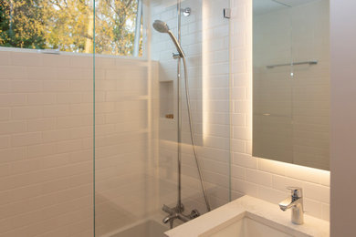 Exemple d'une petite salle de bain tendance en bois foncé avec un placard à porte affleurante, une baignoire en alcôve, un combiné douche/baignoire, WC suspendus, un carrelage blanc, des carreaux de céramique, un mur blanc, un sol en carrelage de céramique, un lavabo encastré, un plan de toilette en quartz modifié, un sol gris, une cabine de douche à porte battante, un plan de toilette blanc, une niche, meuble simple vasque et meuble-lavabo suspendu.