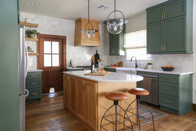 Small traditional u-shaped open plan kitchen in Oklahoma City with a farmhouse sink, shaker cabinets, green cabinets, quartz benchtops, white splashback, porcelain splashback, stainless steel appliances, medium hardwood floors, with island, brown floor and white benchtop.