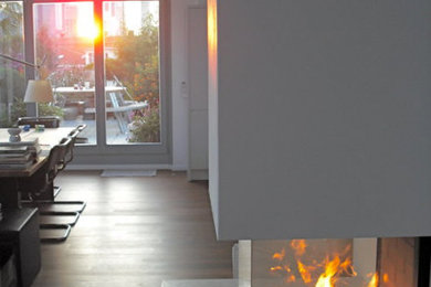 Modernes Wohnzimmer mit Eckkamin, Kaminumrandung aus Beton und braunem Boden in München