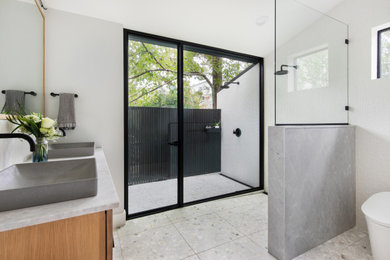 Design ideas for a mid-sized transitional master bathroom in Austin with flat-panel cabinets, light wood cabinets, a curbless shower, a one-piece toilet, white tile, porcelain tile, white walls, terrazzo floors, a vessel sink, engineered quartz benchtops, white floor, an open shower, white benchtops, a niche, a double vanity, a freestanding vanity and vaulted.