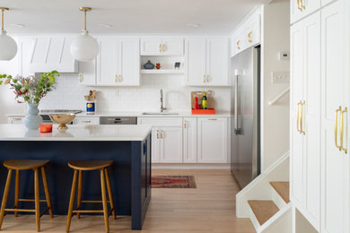 Open concept kitchen - mid-sized transitional l-shaped light wood floor open concept kitchen idea in Detroit with an undermount sink, shaker cabinets, white cabinets, quartz countertops, white backsplash, subway tile backsplash, stainless steel appliances, an island and white countertops