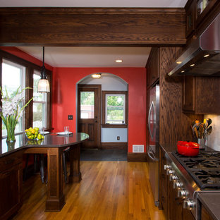 Ejemplo de cocina en U, de estilo americano, pequeña, cerrada, con armarios con paneles empotrados, puertas de armario de madera en tonos medios, electrodomésticos de acero inoxidable, fregadero sobremueble, encimera de cuarzo compacto, salpicadero verde, salpicadero de azulejos de piedra, suelo de madera en tonos medios y península