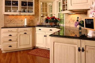 Example of a classic medium tone wood floor kitchen design in Cleveland with raised-panel cabinets, granite countertops, beige backsplash, ceramic backsplash, stainless steel appliances and an island