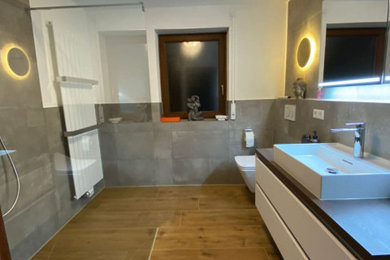 Modernes Badezimmer mit weißen Schränken, bodengleicher Dusche, Wandtoilette, Fliesen in Holzoptik, Aufsatzwaschbecken, grauem Boden, offener Dusche und Einzelwaschbecken in Stuttgart
