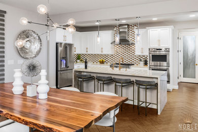 Inspiration for a mid-sized modern l-shaped porcelain tile, beige floor and tray ceiling eat-in kitchen remodel in Las Vegas with an undermount sink, recessed-panel cabinets, white cabinets, quartzite countertops, metallic backsplash, glass tile backsplash, stainless steel appliances, an island and white countertops