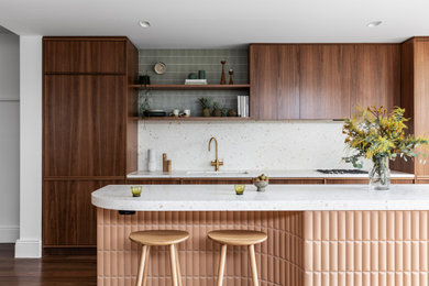 Modern inredning av ett litet rosa rosa kök med öppen planlösning, med en undermonterad diskho, skåp i mellenmörkt trä, bänkskiva i terrazo, rosa stänkskydd, stänkskydd i sten, svarta vitvaror, mellanmörkt trägolv, en köksö och brunt golv