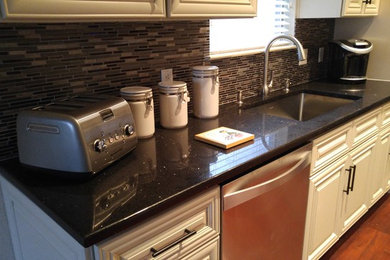 Mid-sized elegant u-shaped dark wood floor enclosed kitchen photo in Austin with an undermount sink, raised-panel cabinets, white cabinets, terrazzo countertops, beige backsplash, glass tile backsplash and stainless steel appliances