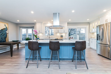 Design ideas for a modern l-shaped eat-in kitchen in Other with an undermount sink, shaker cabinets, white cabinets, quartzite benchtops, white splashback, ceramic splashback, stainless steel appliances, light hardwood floors, with island and white benchtop.