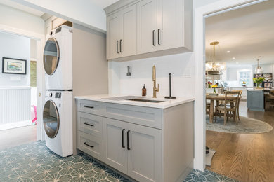 Utility room - mid-sized galley porcelain tile and blue floor utility room idea in New York with an undermount sink, shaker cabinets, gray cabinets, quartz countertops, white backsplash, ceramic backsplash, blue walls, a stacked washer/dryer and white countertops