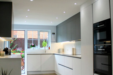 Large modern grey and white l-shaped kitchen/diner in Other with a built-in sink, flat-panel cabinets, quartz worktops, white splashback, engineered quartz splashback, black appliances, vinyl flooring, no island, grey floors, white worktops and feature lighting.