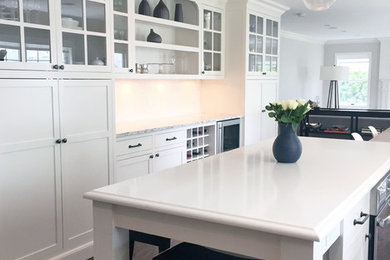 Example of a mid-sized transitional galley dark wood floor and brown floor eat-in kitchen design in New York with shaker cabinets, white cabinets, stainless steel appliances, an island, granite countertops and white backsplash