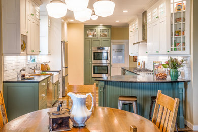 Example of a country u-shaped brown floor eat-in kitchen design in Minneapolis with a farmhouse sink, shaker cabinets, green cabinets, white backsplash, subway tile backsplash, stainless steel appliances, a peninsula and black countertops