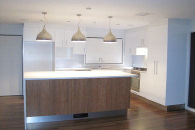 Photo of a modern kitchen in Canberra - Queanbeyan with white cabinets, white splashback, stainless steel appliances and with island.