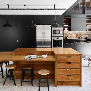 Large industrial kitchen pantry inspiration - Inspiration for a large industrial l-shaped concrete floor kitchen pantry remodel in Sunshine Coast with an undermount sink, black cabinets, wood countertops, brick backsplash, stainless steel appliances and an island