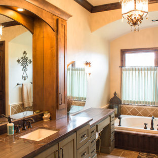 Immagine di una stanza da bagno padronale rustica di medie dimensioni con lavabo sottopiano, vasca da incasso, piastrelle marroni, piastrelle in pietra, pavimento in travertino, ante in stile shaker, ante verdi, pareti beige e top in legno