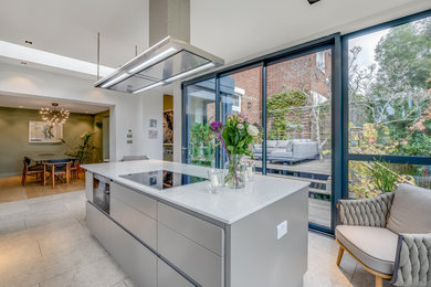 This is an example of a large modern grey and white kitchen in London with a built-in sink, flat-panel cabinets, grey cabinets, composite countertops, white splashback, glass sheet splashback, stainless steel appliances, limestone flooring, an island, grey floors, white worktops, a drop ceiling and feature lighting.