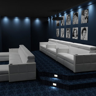 Photo of a large contemporary enclosed home cinema in New York with black walls, carpet, a projector screen and blue floors.