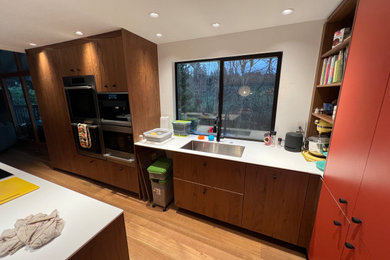 Example of a mid-sized minimalist l-shaped medium tone wood floor and brown floor eat-in kitchen design in Seattle with an undermount sink, flat-panel cabinets, dark wood cabinets, solid surface countertops, paneled appliances, an island and white countertops