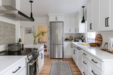 Inspiration for a mid-sized l-shaped light wood floor enclosed kitchen remodel in Portland with an undermount sink, shaker cabinets, white cabinets, quartz countertops, white backsplash, ceramic backsplash, stainless steel appliances, a peninsula and white countertops