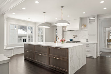 Large traditional galley kitchen/diner in Calgary with a belfast sink, raised-panel cabinets, engineered stone countertops, white splashback, engineered quartz splashback, integrated appliances, dark hardwood flooring, multiple islands, brown floors and white worktops.