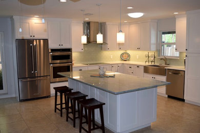 Photo of a large transitional l-shaped eat-in kitchen in Tampa with a farmhouse sink, shaker cabinets, white cabinets, green splashback, porcelain splashback, stainless steel appliances, ceramic floors, with island, beige floor and granite benchtops.