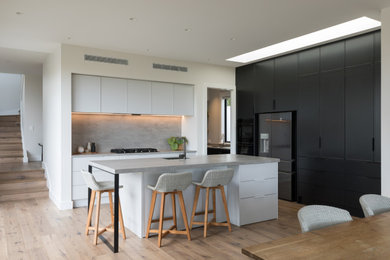Large modern l-shaped eat-in kitchen in Auckland with black appliances and with island.