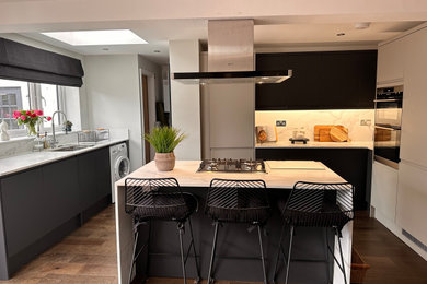 Large modern open plan kitchen in Gloucestershire with an undermount sink, flat-panel cabinets, quartz benchtops, black appliances, dark hardwood floors and with island.