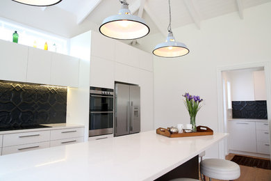 Mid-sized beach style u-shaped kitchen in Auckland with black splashback, medium hardwood floors, with island and brown floor.