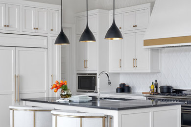 Inspiration for a transitional l-shaped medium tone wood floor and brown floor kitchen remodel in Dallas with an undermount sink, shaker cabinets, white cabinets, white backsplash, paneled appliances, an island and black countertops